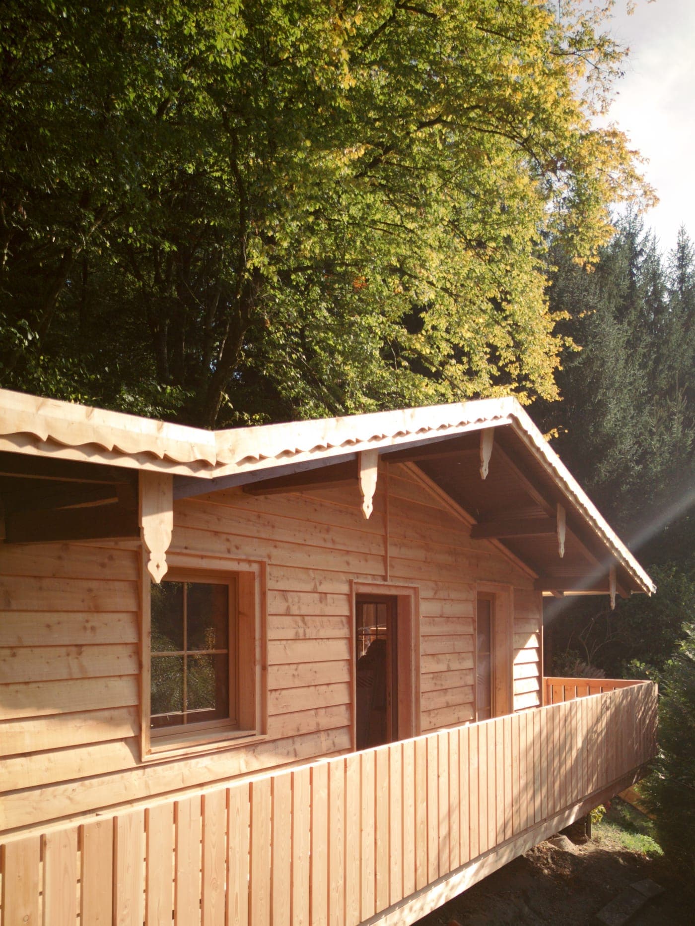 Die Waldraum-Hütte mit Holzbalkon und verzierten Giebelbrettern unter goldenen Herbstbäumen